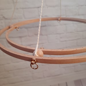 Può includere: Un mobile a cerchio in legno con due cerchi, un cordoncino bianco e una perla di legno. I cerchi sono collegati da anelli di metallo dorati.