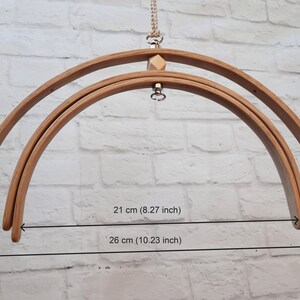 May include: Two wooden hoops, one 21 inches in diameter and the other 26 inches in diameter, are hanging from a white brick wall. The hoops are connected by a metal ring and a wooden bead.