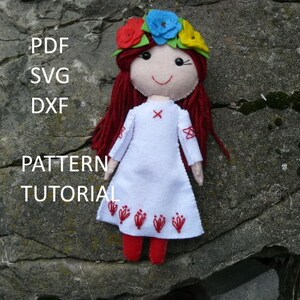 Könnte beinhalten: Handgemachte Filzpuppe mit roten Garnhaaren und einem Blumenkranz. Die Puppe trägt ein weißes Kleid mit roten Stickereien und rote Schuhe. Der Text lautet "PDF SVG DXF PATTERN TUTORIAL".
