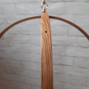 May include: A wooden mobile hanger with a circular shape and a hole in the center. The hanger is made of natural wood and has a light brown color.