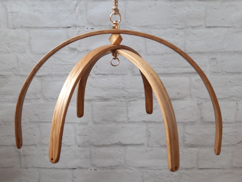 May include: A wooden mobile frame with three curved wooden arches. The frame is made of natural wood and has a gold metal ring at the top.