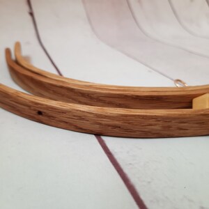 May include: Three wooden embroidery hoops of different sizes, nested together. The hoops are made of natural wood with a light brown finish. A gold-colored metal ring is attached to the largest hoop.