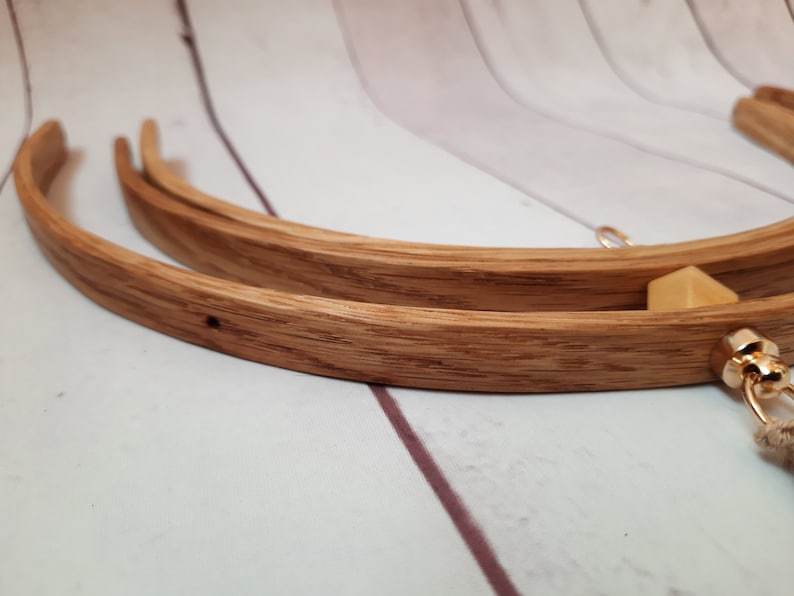 May include: Three wooden embroidery hoops of different sizes, nested together. The hoops are made of natural wood with a light brown finish. A gold-colored metal ring is attached to the largest hoop.