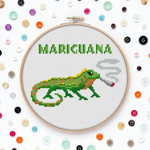 May include: A cross-stitch embroidery hoop featuring a green iguana smoking a cigarette. The text "MARIJUANA" is above the iguana.