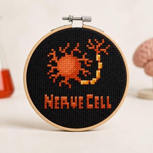 May include: A circular wooden embroidery hoop containing black fabric with a cross-stitched orange and yellow nerve cell design. Below the nerve cell, the text NERVE CELL is stitched in orange and yellow block letters on the black fabric background.