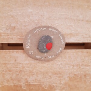 May include: A round, gray stone with a painted robin on it. The stone has the text "Robins appear when loved ones are near" written around the edge.