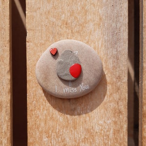 Puede incluir: Una piedra gris pintada con un petirrojo y las palabras "Te echo de menos". Un peque&ntilde;o coraz&oacute;n rojo est&aacute; pintado sobre el petirrojo.