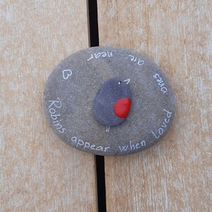 May include: A gray stone painted with a robin and the words "Robins appear when loved ones are near".