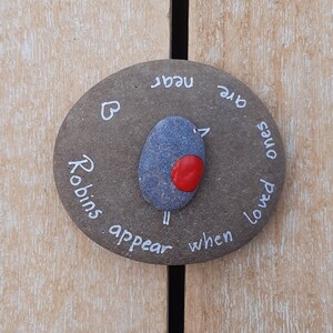 May include: A gray stone with white lettering that reads "When loved ones are near, Robins appear". A small painted bird with a red breast is in the center of the stone.