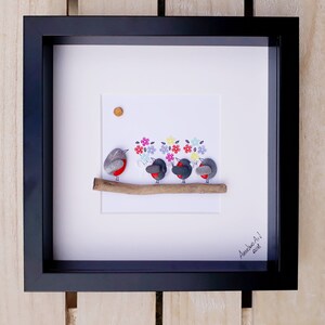 May include: Framed artwork featuring a pebble art design of five robins perched on a branch with a background of colorful flowers. The artwork is signed "Anselmo Art! 2018".