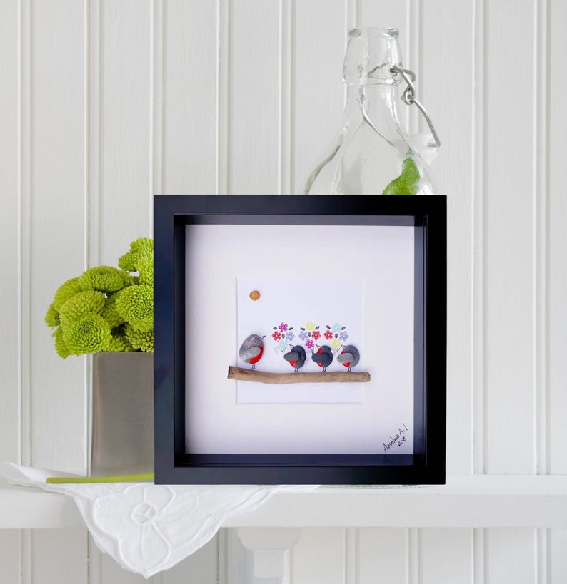May include: A framed artwork featuring a pebble art design of four robins perched on a branch with colorful flowers behind them. The artwork is signed "Amanda Art" and dated 2018.