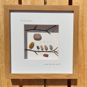 May include: Framed artwork featuring a hand-painted pebble art scene of five birds perched on a branch. The birds are singing and a sign that says "Music" hangs from the branch. The text "The best teachers... teach from the heart!" is written below the scene.
