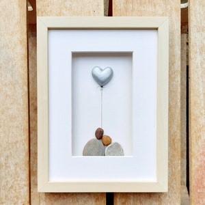 May include: A framed artwork featuring a silver heart-shaped balloon floating above a stack of gray, brown, and orange stones.