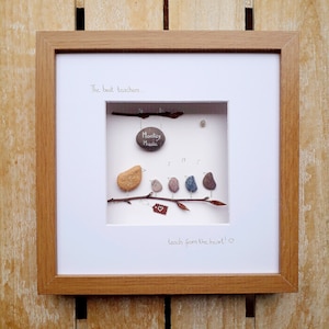 May include: Framed artwork featuring a pebble art design of five birds perched on a branch. The birds are singing and one holds a sign that says "Monkey Music". The text "The best teachers... teach from the heart!" is written below the birds.