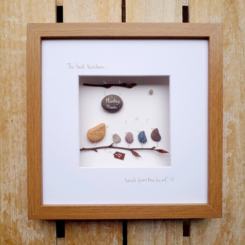May include: Framed artwork featuring a pebble art design of five birds perched on a branch. The birds are singing and one holds a sign that says "Monkey Music". The text "The best teachers... teach from the heart!" is written below the birds.