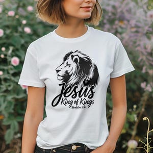 Puede incluir: Camiseta blanca con un gráfico de león negro y el texto "Jesús Rey de Reyes Apocalipsis 19:16".