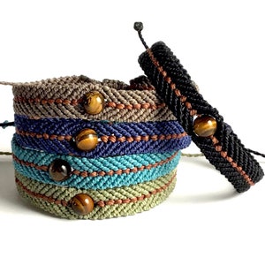 May include: A stack of macrame bracelets in various colors, including gray, navy blue, teal, and olive green. Each bracelet features a central decorative band and a tiger's eye bead. A black bracelet with a similar design is displayed separately.