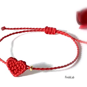 Peut inclure: Bracelet rouge avec un cœur en crochet et un fermoir coulissant réglable. Le bracelet est orné d'une petite perle dorée et est fait de cordon rouge. Le cœur est au centre du bracelet.