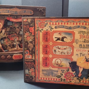 May include: Two decorative boxes with a vintage circus theme. One box features a miniature stage with a clown, while the other displays ticket stubs and circus imagery. The boxes are brown with red, orange, and floral accents, and the text "COME ONE + COME ALL" is visible.