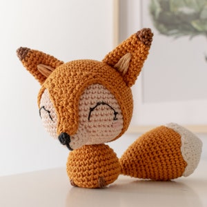 May include: A crocheted fox toy with a brown and orange body, a white tail tip, and a pink face with black eyes.
