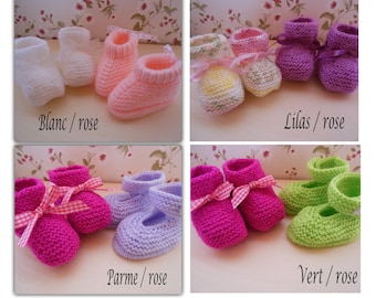 Op de afbeelding: Vier paar gebreide babyschoentjes in verschillende kleuren: wit, roze, paars en groen. Elk paar heeft een roze strik.