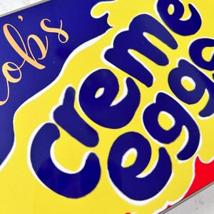 May include: A close-up of a yellow and blue box with the words "Creme Eggs" in a white outline. The box has a red and white border.