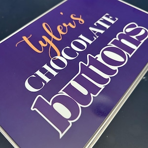 May include: A purple tin with white lettering that reads "Tyler's Chocolate Buttons". The text "Tyler's" is in orange.