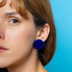 Könnte beinhalten: Eine Frau mit braunen Haaren trägt große, runde, blaue Ohrringe.