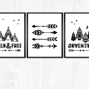Puede incluir: Tres impresiones de arte de pared imprimibles en blanco y negro con un tema de bosque. La primera impresión presenta una luna creciente, estrellas y tres tipis con patrones geométricos. La segunda impresión presenta cinco flechas blancas y negras. La tercera impresión presenta una luna creciente, estrellas y cinco árboles con patrones geométricos. El texto "WILD & FREE" está en la primera impresión y "ADVENTURE" está en la tercera impresión.