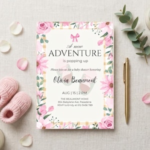 Puede incluir: Una invitación a un baby shower con detalles florales y lazos. La invitación dice "A new adventure is popping up" e incluye el nombre Olivia Beaumont. También hay patucos rosas, un bolígrafo dorado y velas.