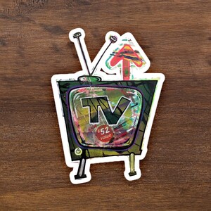 Puede incluir: Un televisor de estilo vintage con un marco verde y negro, una pantalla colorida con las letras "TV" y un círculo rojo con el texto "52 € de valor". El televisor tiene dos antenas y una flecha roja apuntando hacia arriba.