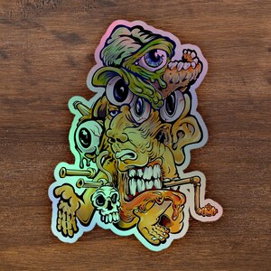 Könnte beinhalten: Ein farbenfroher Sticker mit einer grotesken, mehräugigen Kreatur mit einer tropfenden, klebrigen Textur. Die Kreatur hat einen großen, zahnigen Mund und scheint einen Hut zu tragen. Der Sticker ist im psychedelischen Stil mit leuchtenden Farben und filigranen Details gestaltet.