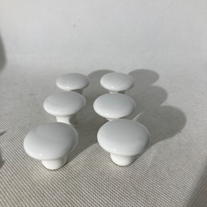 May include: Six white cabinet knobs with a rounded top and a short, cylindrical base. The knobs are arranged in two rows of three, against a white background. The knobs are made of a glossy material.