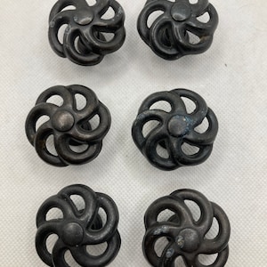 May include: Six dark bronze-colored cabinet knobs with a flower-like design. Each knob features a central circular element surrounded by six curved, petal-shaped arms. The knobs are arranged in two rows of three.