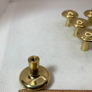 以下が含まれることがあります： 丸みを帯びたデザインの真鍮製キャビネットノブのセット。ノブは木製の定規と一緒に表示され、直径は約2.5cmです。