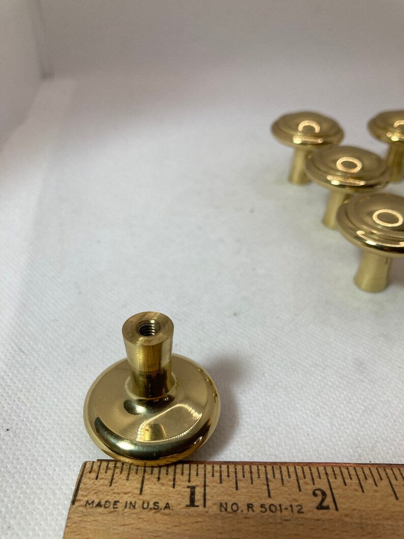 以下が含まれることがあります： 丸みを帯びたデザインの真鍮製キャビネットノブのセット。ノブは木製の定規と一緒に表示され、直径は約2.5cmです。