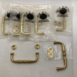May include: Several pieces of decorative hardware, including drawer pulls and hooks, in a polished brass finish. The hardware is packaged in clear plastic bags with the "TOP KNOBS" logo and text. The hardware includes screws and washers.