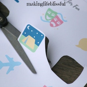 K&ouml;nnte beinhalten: Schere schneidet Papier mit einem Camping-Symbol. Das Symbol zeigt ein Zelt unter einem Nachthimmel mit Mond und Sternen. Weitere Symbole sind ein Flugzeug, W&uuml;rfel und Sprechblasen. Der Text "makinglifeblissful" ist sichtbar.