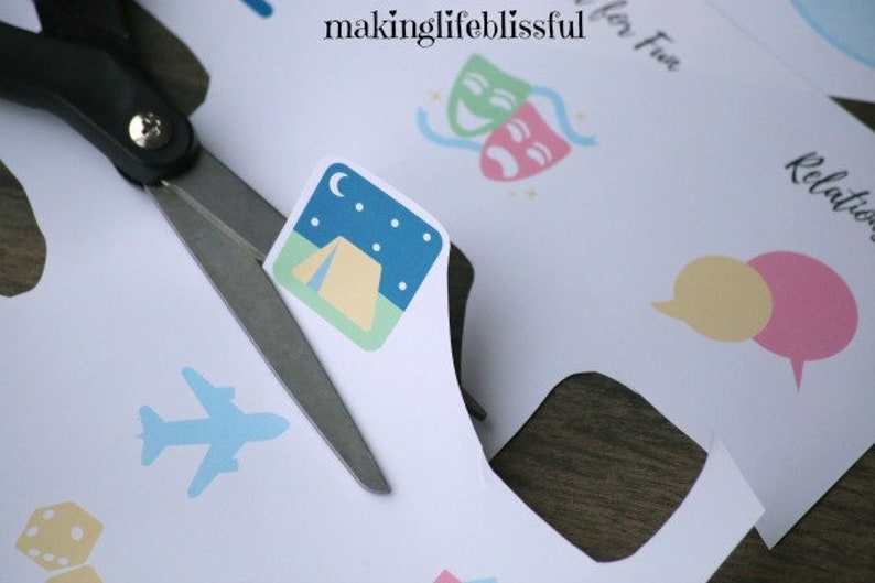 K&ouml;nnte beinhalten: Schere schneidet Papier mit einem Camping-Symbol. Das Symbol zeigt ein Zelt unter einem Nachthimmel mit Mond und Sternen. Weitere Symbole sind ein Flugzeug, W&uuml;rfel und Sprechblasen. Der Text "makinglifeblissful" ist sichtbar.