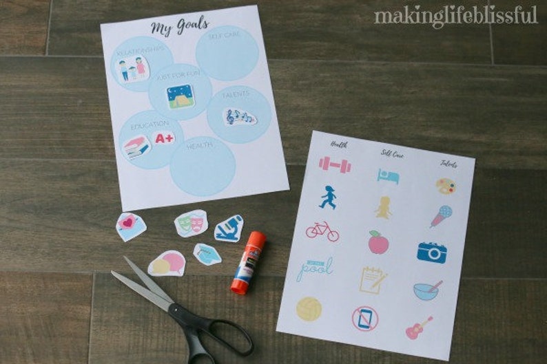 K&ouml;nnte beinhalten: Zwei Bl&auml;tter Papier mit den W&ouml;rtern "My Goals" und "Health, Self Care, Talents" aufgedruckt. Das "My Goals"-Blatt hat Kreise mit Symbolen. Das andere Blatt hat Symbole f&uuml;r Gesundheit, Selbstpflege und Talente. Es gibt Aufkleber, eine Schere und Klebstoff.