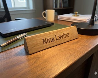 May include: A triangular wooden desk nameplate featuring the engraved text Nina Lavina. The nameplate is crafted from light-toned wood with a visible grain, displaying a smooth, angled front surface that clearly shows the dark, laser-etched lettering.