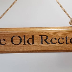 May include: Wooden sign with the text "The Old Rectory" engraved in a dark font. The sign is rectangular, made of light brown wood, and hangs from a natural rope. The sign is a decorative item.