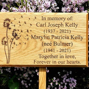 May include: A wooden memorial plaque with a dandelion design and the text "In memory of: Carl Joseph Kelly (1937-2021) Marylin Patricia Kelly (neé Bulmer) (1941-2021) Together in love, Forever in our hearts."