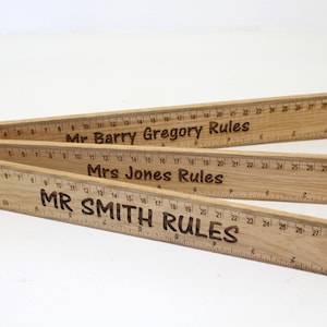 Könnte beinhalten: Vier Holzlineale mit den Namen "Mr. Barry Gregory", "Mrs Jones" und "Mr Smith", gefolgt vom Wort "Rules", das auf jedes Lineal graviert ist.