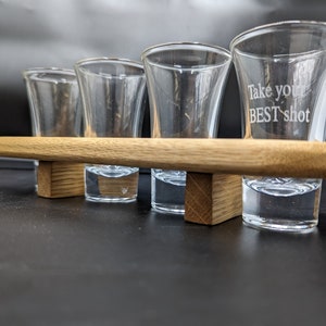 May include: Four clear shot glasses on a wooden tray. The glass on the right has the text "Take your BEST shot" etched into it.