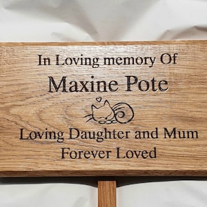 Może przedstawiać: Drewniana tablica pamiątkowa z napisem "In Loving memory Of Maxine Pote Loving Daughter and Mum Forever Loved." Ilustracja kota znajduje się pomiędzy imieniem a tekstem. Tablica jest jasnobrązowa z ciemniejszą obwódką.