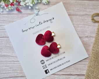 May include: Two burgundy velvet heart-shaped hair clips with gold accents. The clips are on a white card with the text "bow sew cute designs" and website information.