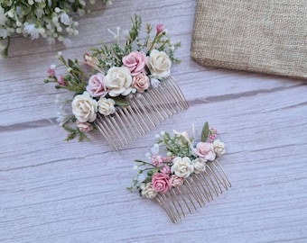 May include: Two floral hair combs with pink and white flowers and greenery. The combs are on a light wood background. The text "handmade with love" is visible on a burlap bag in the background.