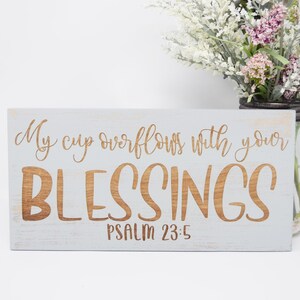 May include: A light blue wooden sign with the text "My cup overflows with your BLESSINGS Psalm 23:5" in brown lettering.