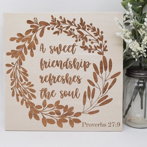 May include: A wooden sign with a brown floral wreath design and the text "A sweet friendship refreshes the soul" with the scripture reference "Proverbs 27:9" below.